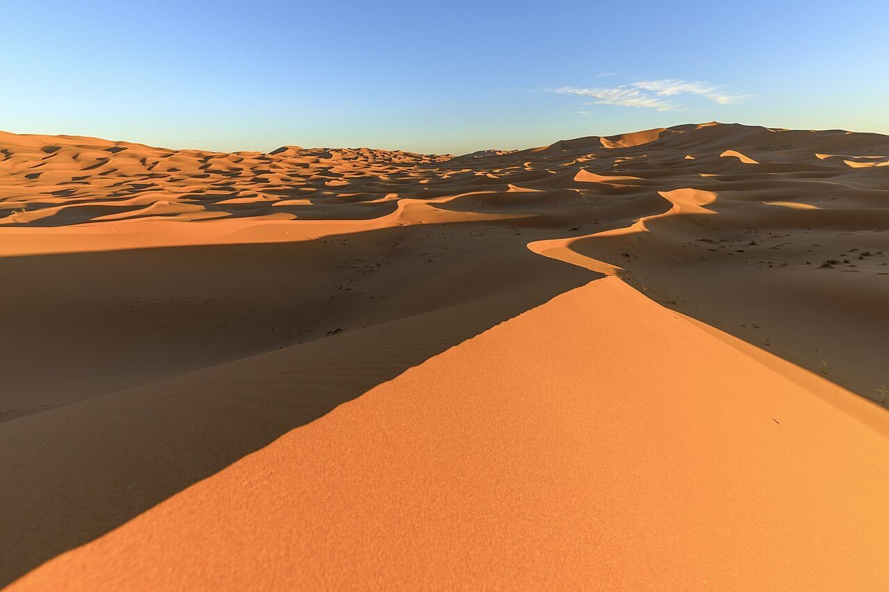 Towering orange Erg Chebbi sand dunes with sharp ridgelines near Merzouga under a clear blue sky