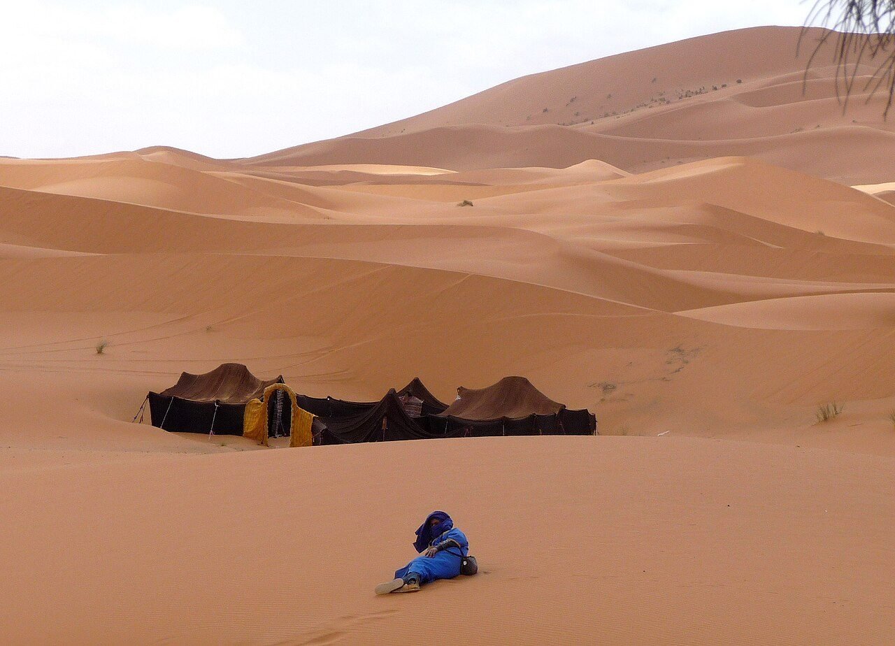 Lit white luxury tents with rugs and lanterns at a desert camp among the Erg Chebbi dunes near Merzouga at dusk
