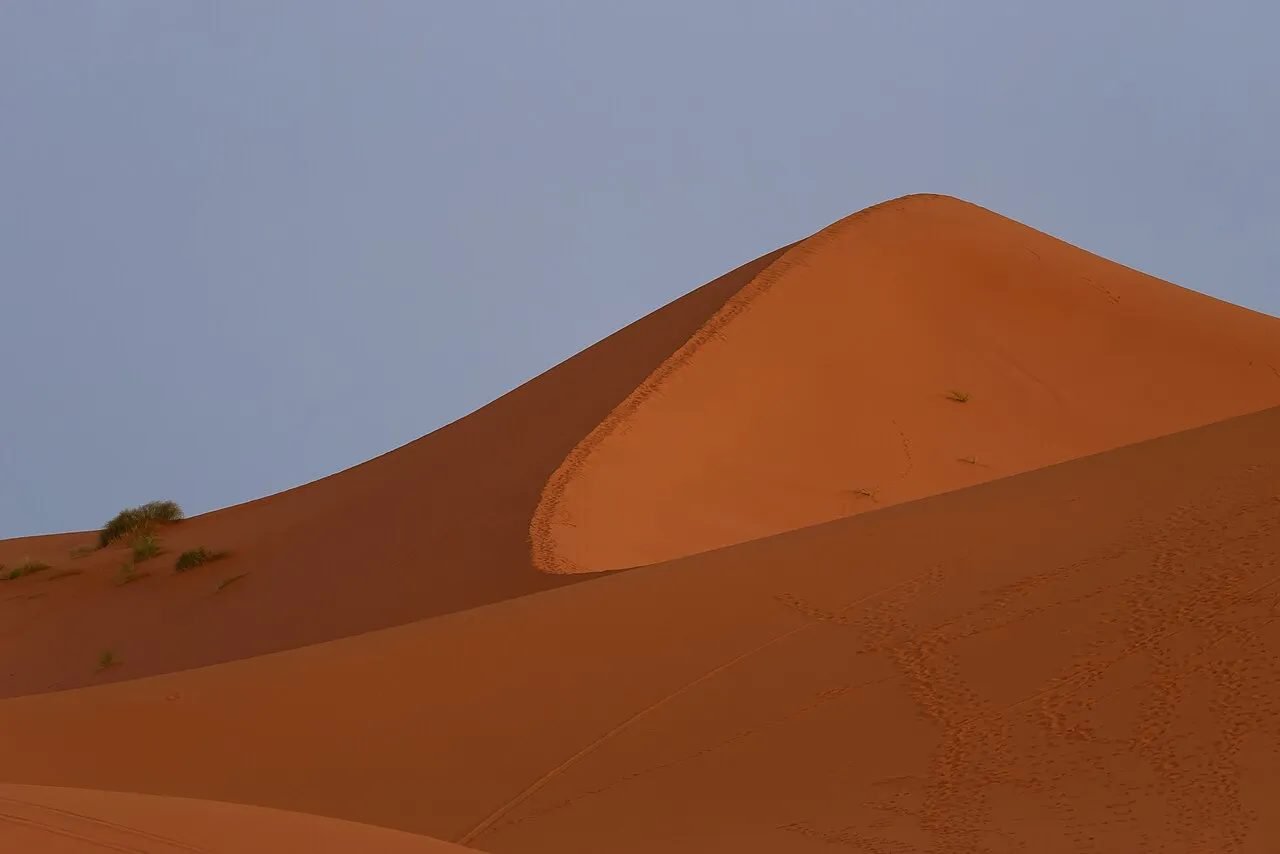 Traveller sandboarding down an orange dune in Erg Chebbi near Merzouga